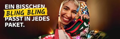 Eine Frau nimmt einen Weihnachtspullover aus einem Paket. Im Hintergrund ist es weihnachtlich geschmückt. Schriftzug: Ein bisschen Bling Bling passt in jedes Paket.