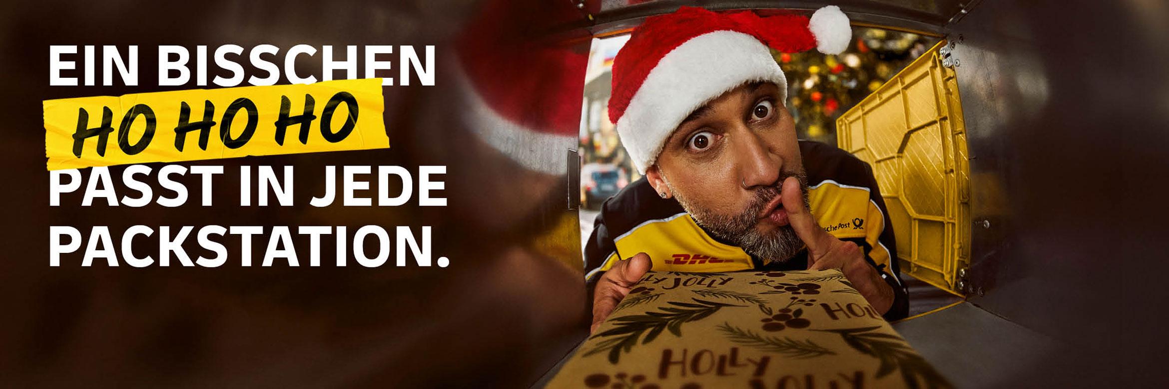 Ein DHL Zusteller mit Weihnachtsmütze legt ein Paket in ein Packstation-Fach. Schriftzug: Ein bisschen Ho Ho Ho passt in jede Packstation.